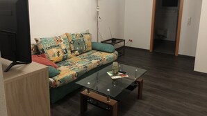 A living room with a sofa, a coffee table, a TV, and a lamp. - Ferienwohnungen Popp (Clausen)