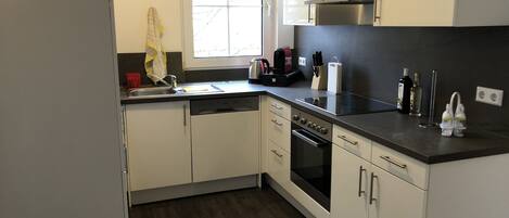 A modern kitchen with white cabinetry, a dishwasher, an oven, and a window providing natural light.