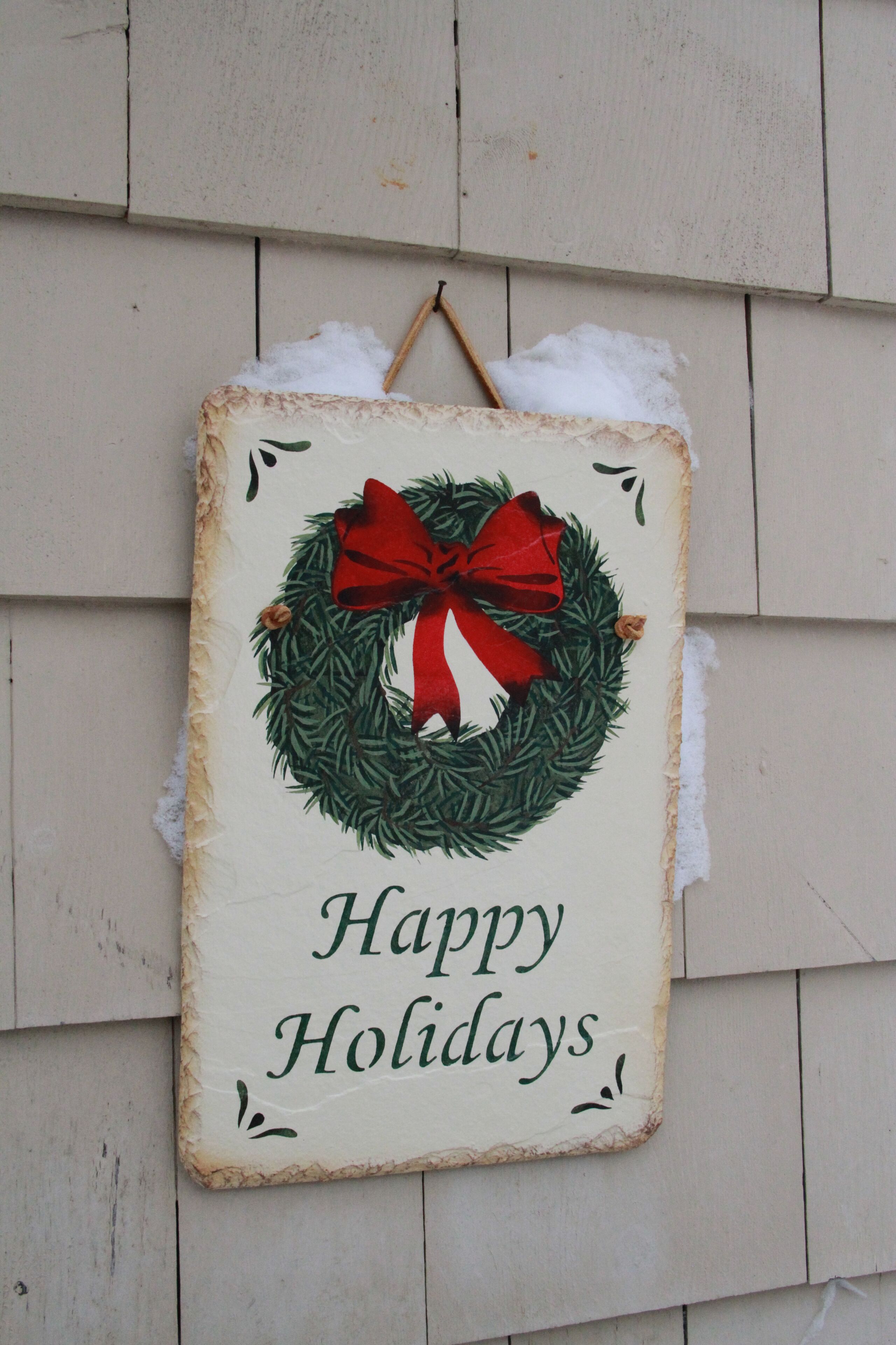 A holiday sign with a red bow and green wreath on a wooden wall.