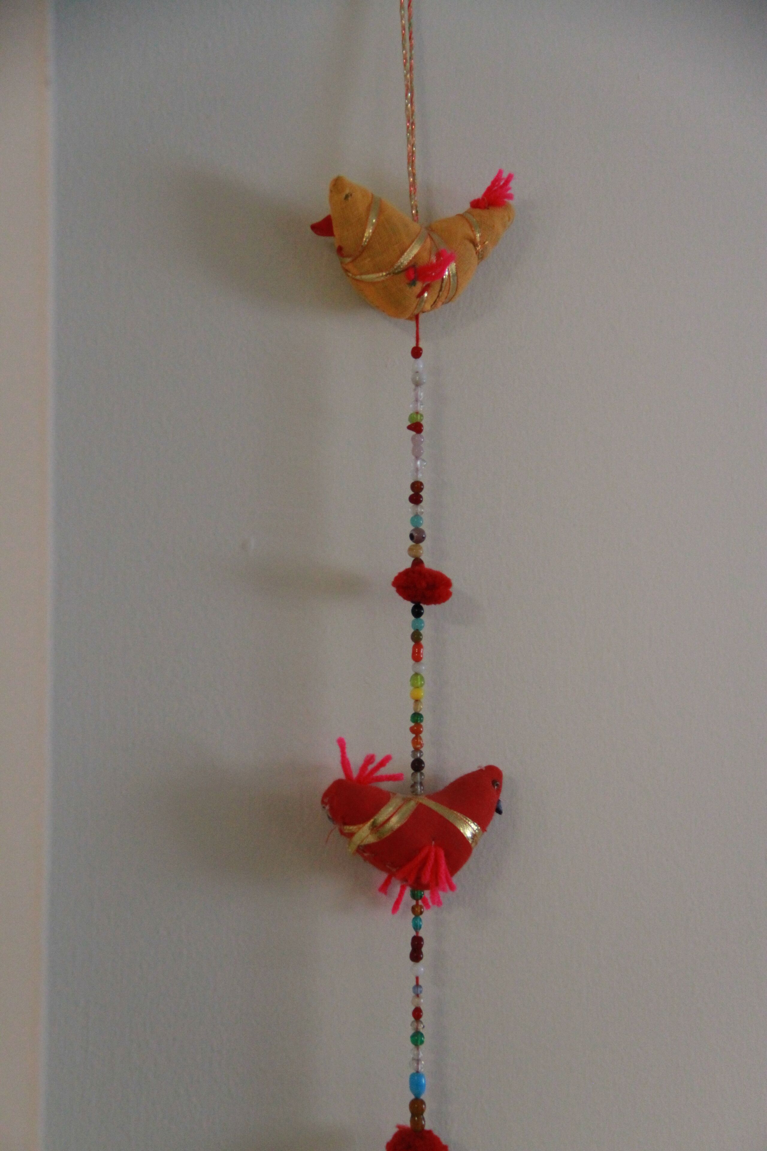 Een verticale reeks decoratieve objecten, waaronder een vogel en kralen.