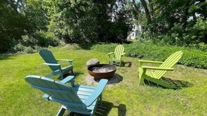 Un'area verde all'aperto con quattro poltrone Adirondack, una delle quali è blu, e un braciere al centro.