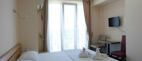 Habitación de hotel con cama, escritorio, silla, televisor y ventana con cortinas.