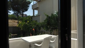 A balcony with a white table and chairs, overlooking a garden with various plants and a building in the background. - Kilic Motel (Arnavutköy)