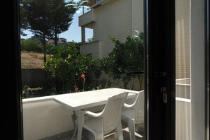 A balcony with a white table and chairs, overlooking a garden with various plants and a building in the background. - Kilic Motel (Arnavutköy)