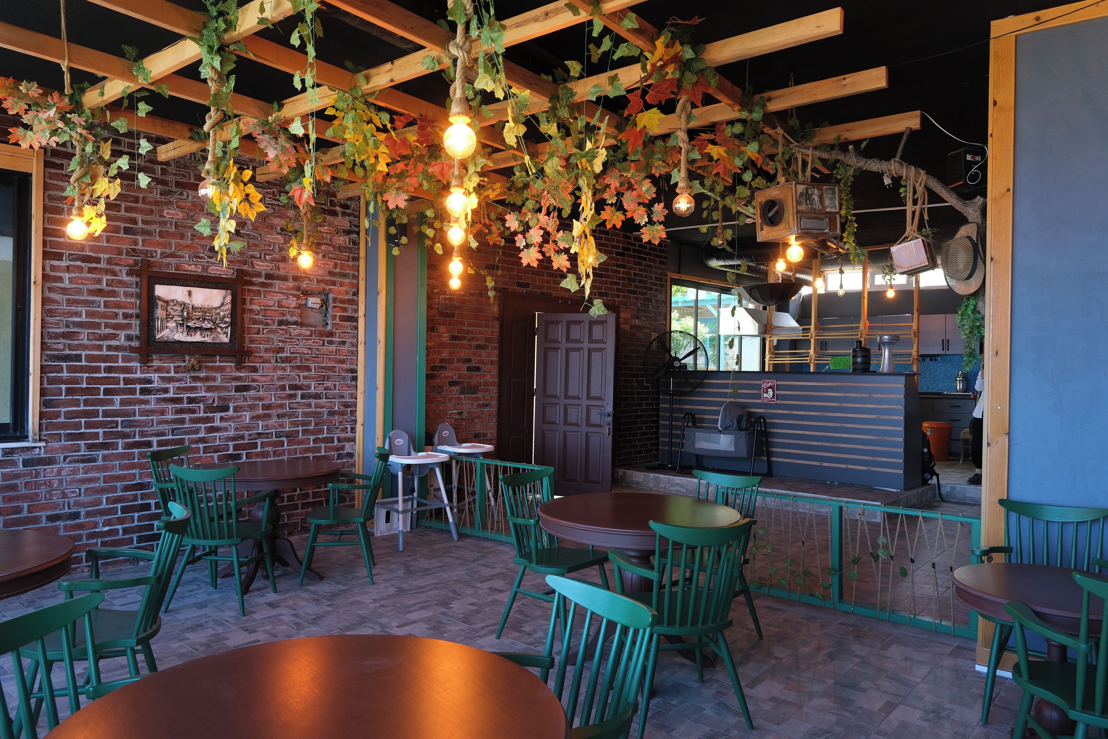 A restaurant interior with brick walls, hanging lights, and green chairs.