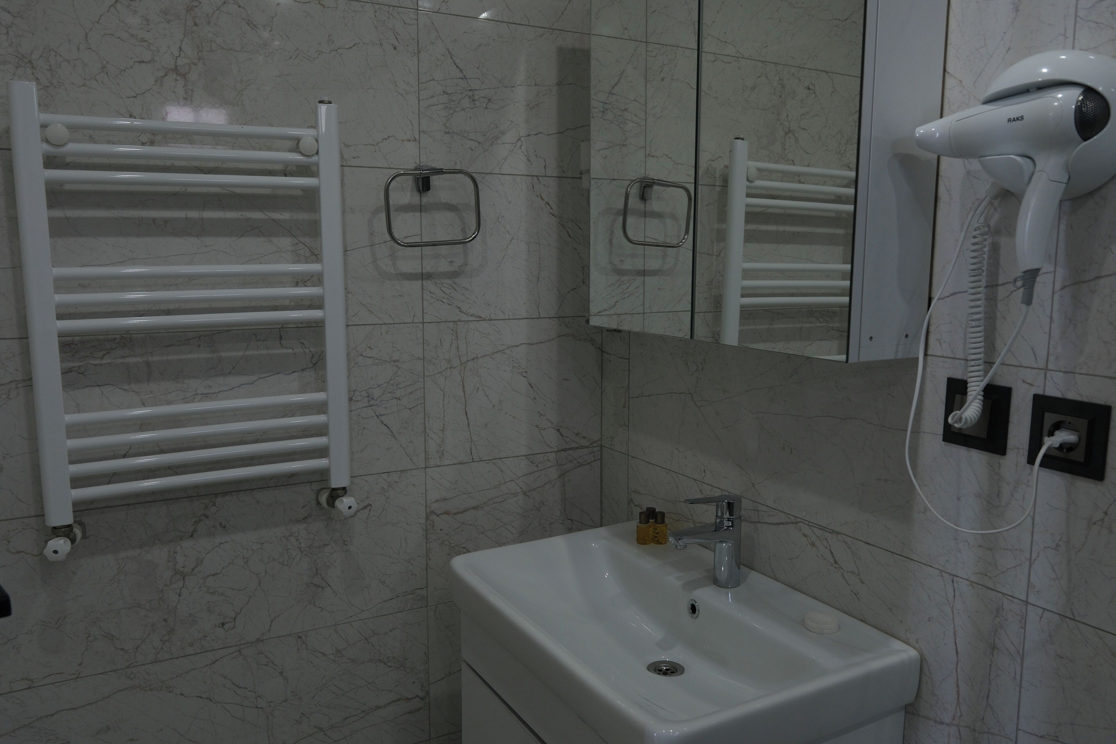 Une salle de bain avec un lavabo blanc, un miroir, un porte-serviettes et un sèche-cheveux.