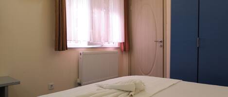 A hotel room with a bed, a radiator, a door, and a window with curtains.