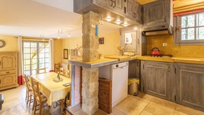 A kitchen with a stone column, wooden cabinets, a dining table, and a red stove. - Les Oliviers - Great value for money! (Saint-Maximin)