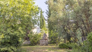 A stone structure in a lush garden with dense foliage and a clear sky. - Les Oliviers - Great value for money! (Saint-Maximin)