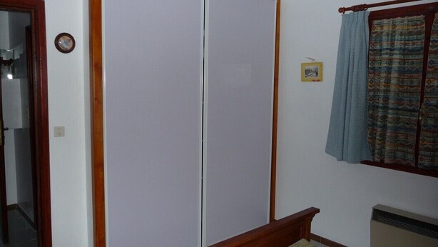 Une chambre à coucher avec un lit, une armoire, une fenêtre avec des rideaux et un radiateur.