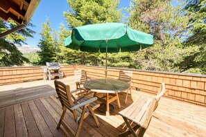 Une terrasse extérieure avec une table et des chaises en bois, un parasol vert et un barbecue.
