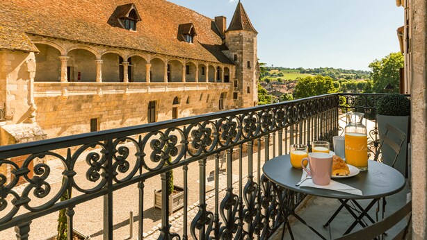 A balcony with a table set for breakfast, overlooking a historic building with arches and a tower.
