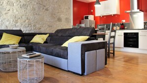 A modern living room with a sofa, two side tables, and a kitchen area with red walls and white cabinets.