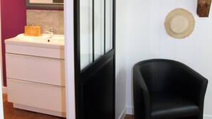 A bathroom with a white vanity, a black chair, and two woven hats on the wall.