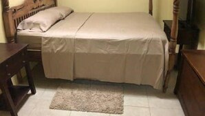 A bedroom with a four-poster bed, a wooden nightstand, a television, and a small rug on the tiled floor. - Nature's Comfortable Suite (East End)