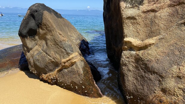 Una costa rocosa con agua cristalina y montañas a lo lejos.