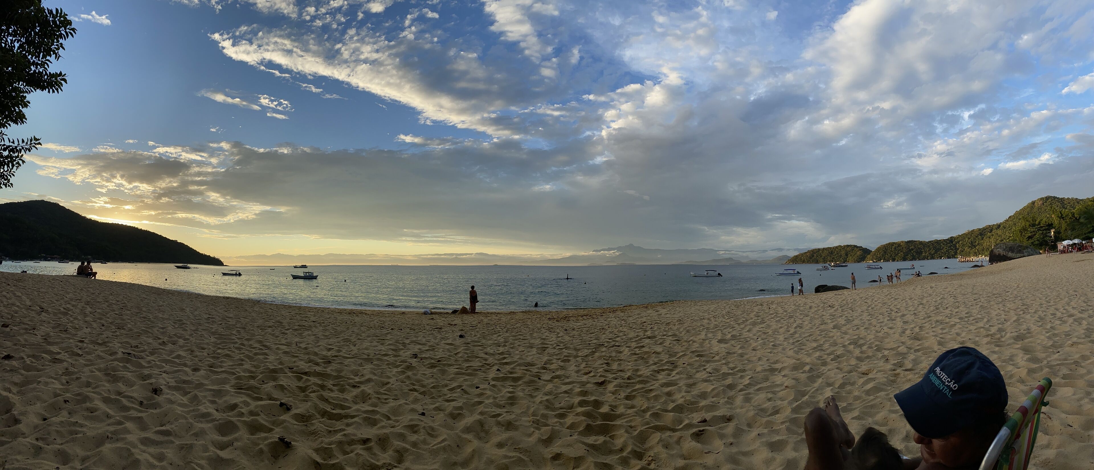 A beach with boats, people, and hills in the background.