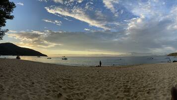 A beach with boats, people, and hills in the background.