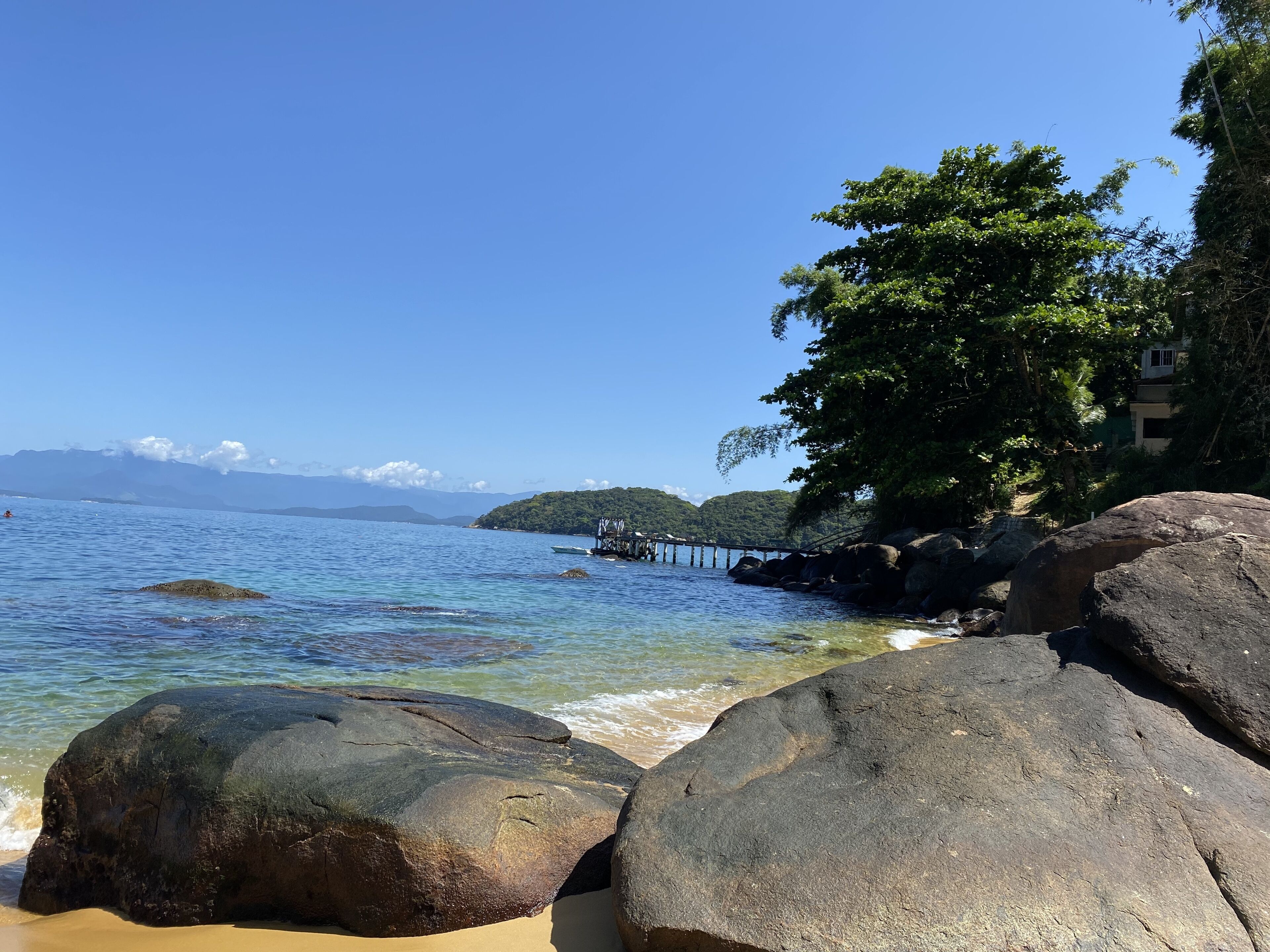 Una spiaggia con grandi rocce, acqua cristallina e un'isola in lontananza.