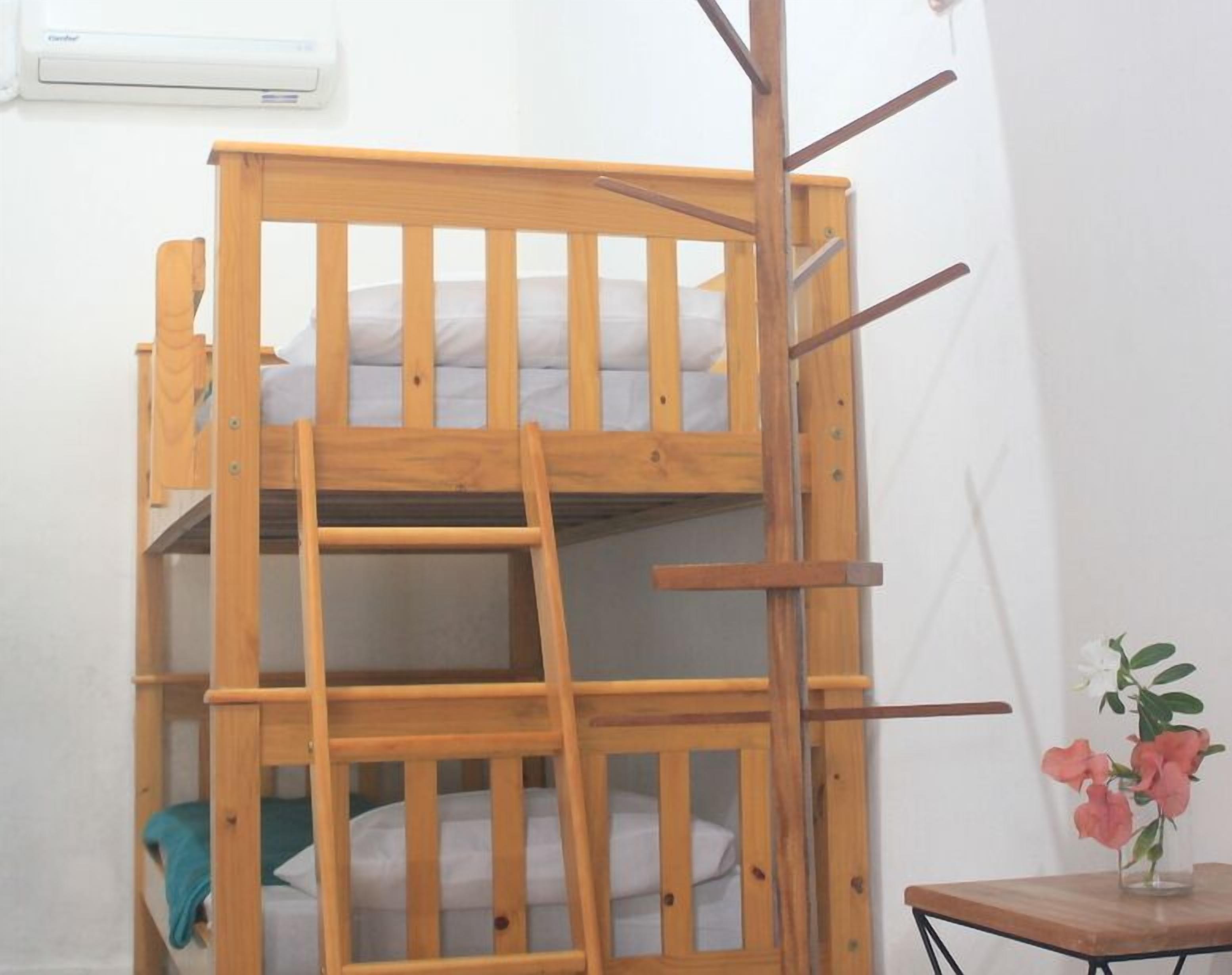 Una cama litera con escalera, una mesita con un florero y un equipo de aire acondicionado en la pared.