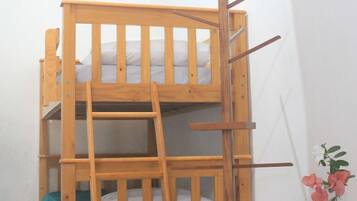 Una cama litera con escalera, una mesita con un florero y un equipo de aire acondicionado en la pared.