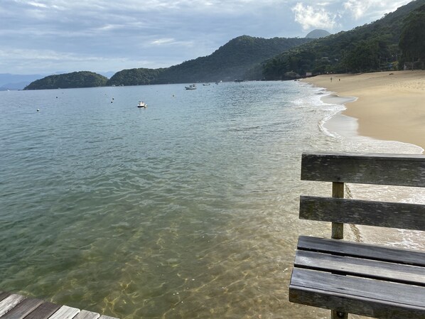 A wooden bench overlooking a beach with clear water and boats. - Suítes Maravilha de Ará (Angra dos Reis)
