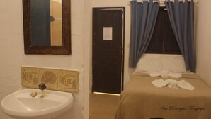 Una habitación pequeña y sencilla con cama, lavamanos y puerta.