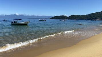 Una playa con agua cristalina, barcos y montañas a lo lejos.