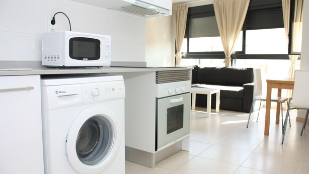 Een praktische keuken met een wasmachine, magnetron en oven. Er is een klein zithoekje met een tafel en stoelen.