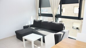 Een moderne woonkamer met een grijze hoekbank, een witte salontafel en een houten bijzettafeltje.