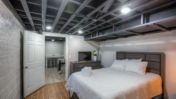 Un dormitorio con cama, mesita de noche, televisor y baño visible a través de una puerta abierta.