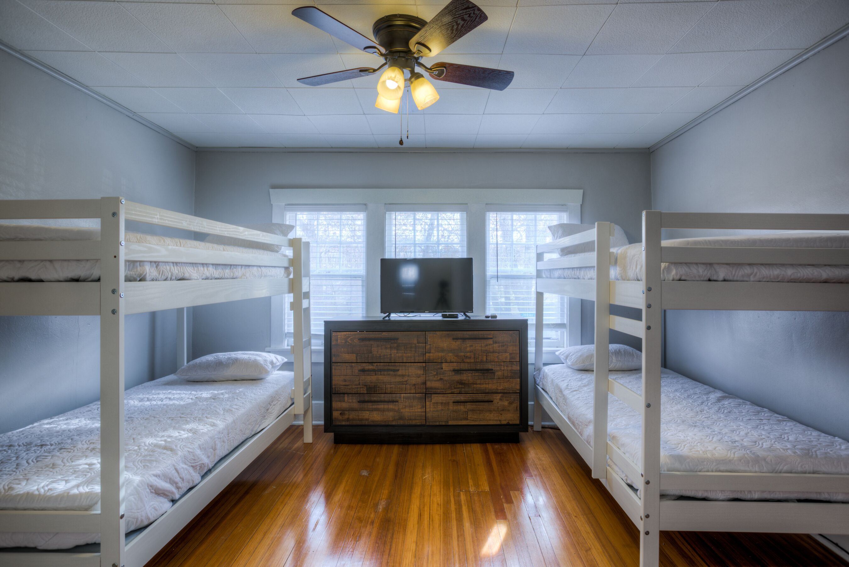 Ein Zimmer mit Etagenbetten, einer Holzkommode und einem Deckenventilator.