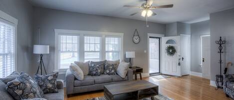 A spacious living room with a grey sofa, a wooden coffee table, and a ceiling fan.