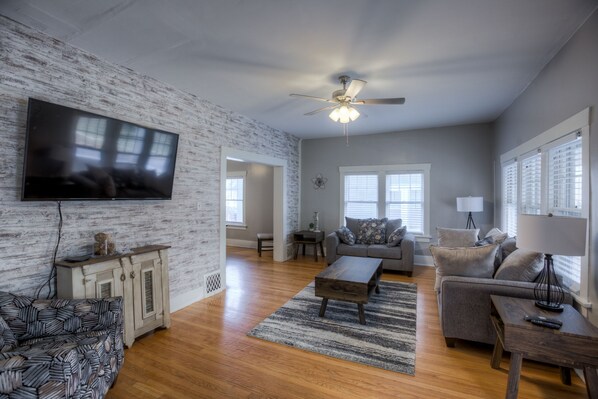 A spacious living room with a large flat-screen TV, a ceiling fan, and a wooden coffee table. - Big Midtown Home! Sports Room, Bunk Beds! (Omaha)