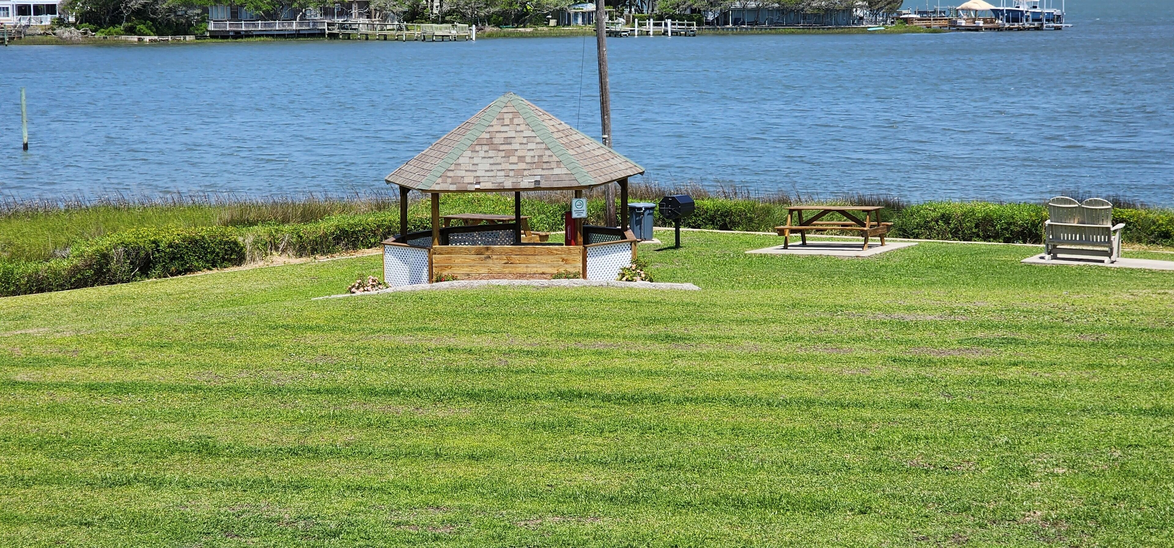 A gazebo with a tiled roof, a picnic table, and a bench by a lake.