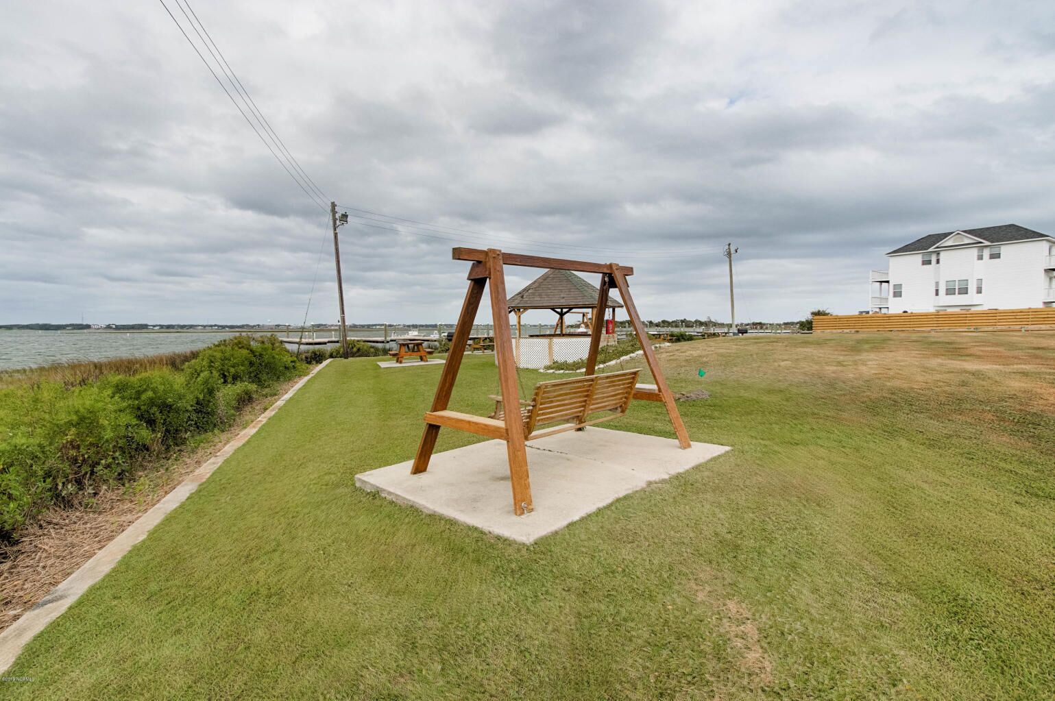 A swing set in a grassy area with a view of the water and a white building in the background.