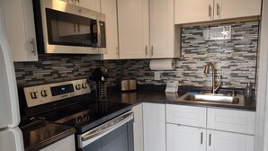 Una cocina moderna con armarios blancos, un microondas de acero inoxidable, horno empotrado, pileta de acero inoxidable y un salpicadero con diseño.