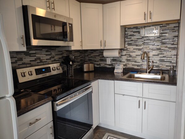 A modern kitchen with white cabinets, a stainless steel microwave, a built-in oven, a stainless steel sink, and a patterned backsplash.
