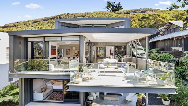 Une maison moderne à deux étages, dotée d’un balcon en verre, d’un escalier et offrant une vue sur la verdure environnante.