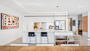 Une cuisine moderne avec des meubles blancs, un îlot central doté de tabourets et un coin repas avec une table en bois.