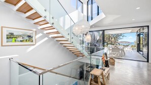 Un intérieur moderne avec un escalier en verre, un coin repas offrant une vue sur l’extérieur et une œuvre d’art encadrée au mur.