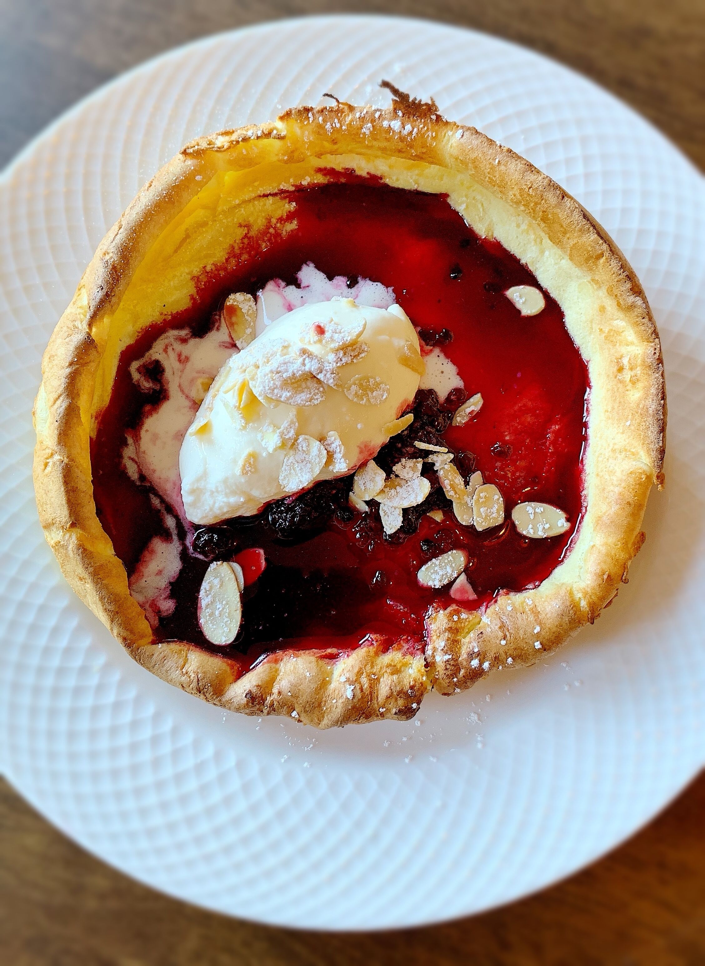 Un dessert composé d’une croûte, d’une garniture rouge et d’une boule de crème glacée, le tout présenté sur une assiette blanche.