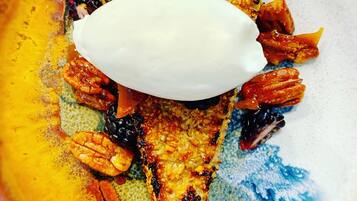A plate with a piece of grilled meat, pecans, and a dollop of white sauce.