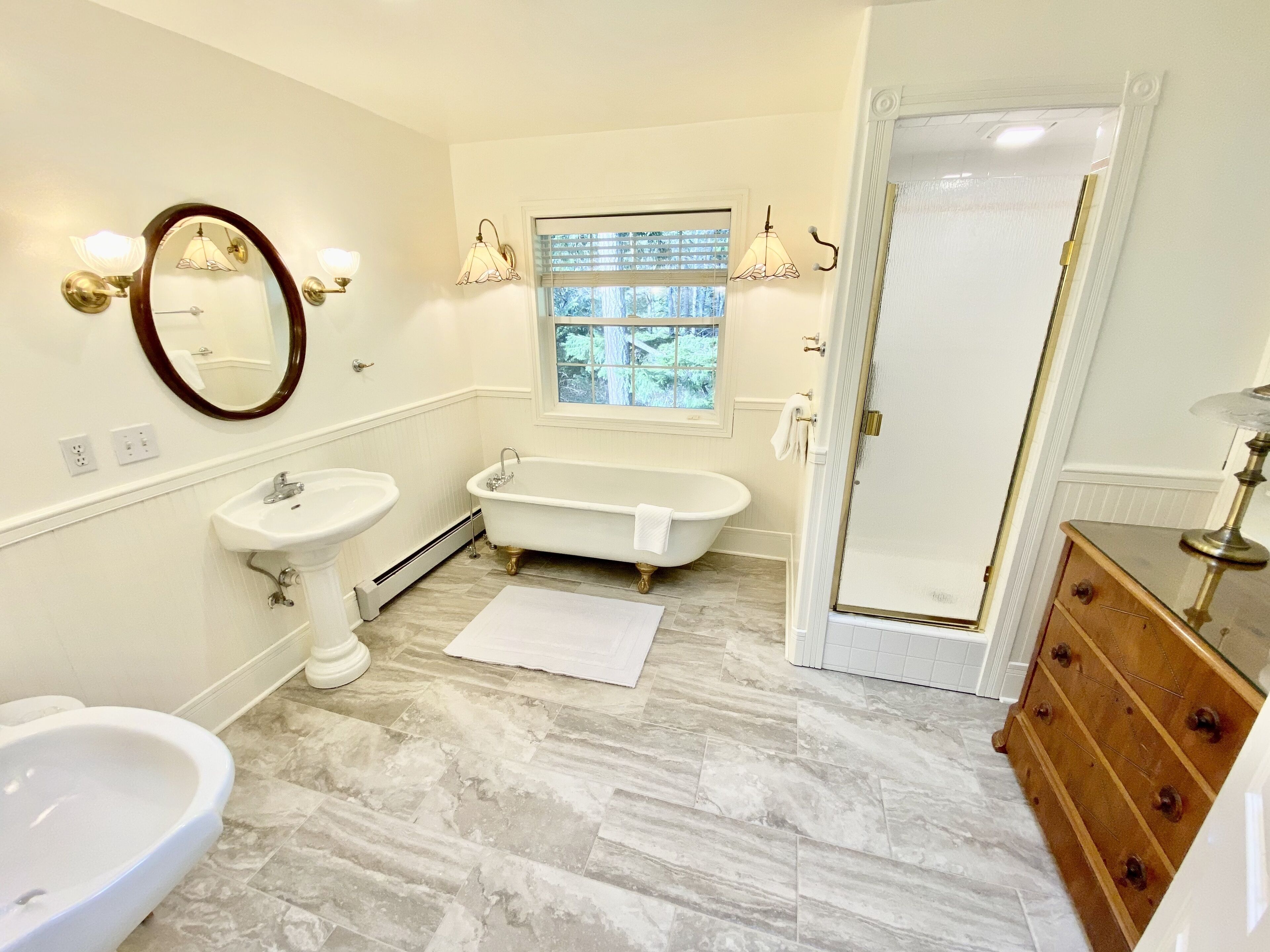 Une salle de bain avec une baignoire sur pieds, un lavabo sur colonne et une coiffeuse avec un miroir.