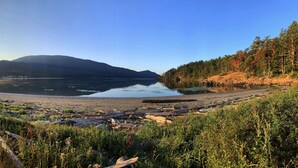 A natural landscape with a lake, forested hills, and a beach.