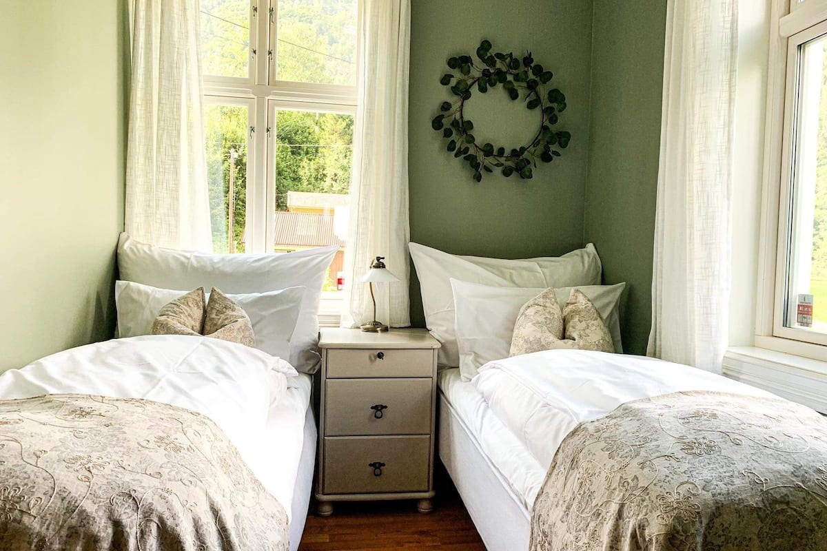 A bedroom with two beds, a nightstand, a lamp, and a wall decoration.