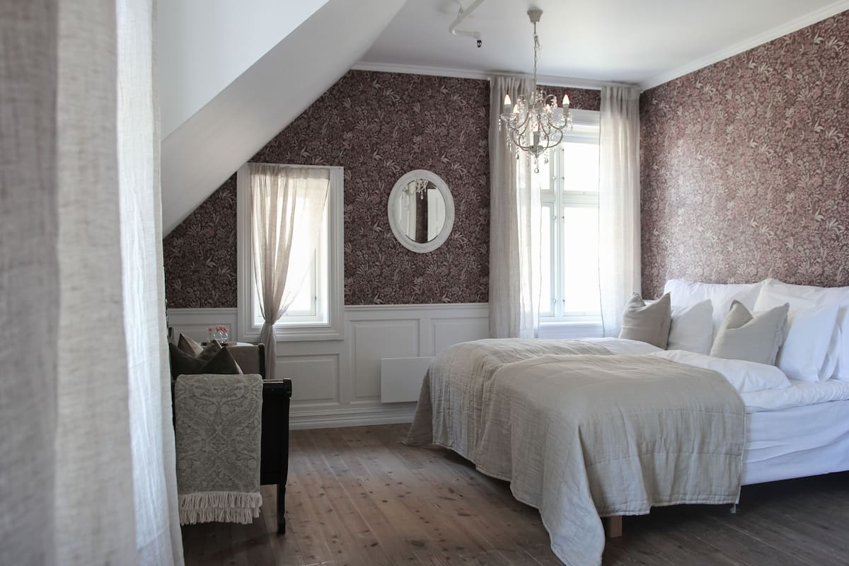 A bedroom with a sloped ceiling, a large bed, a chandelier, and a mirror on the wall.