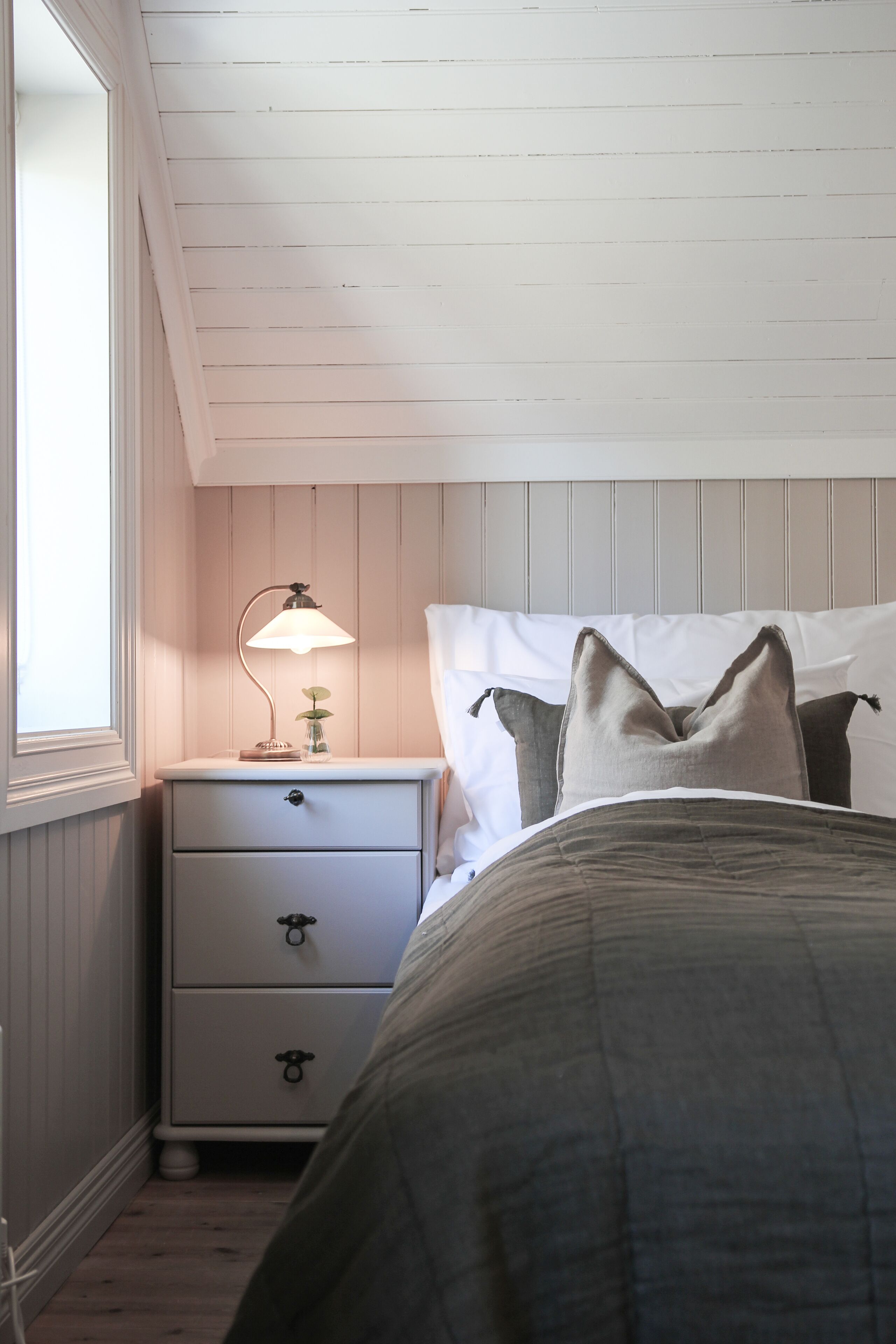 Een slaapkamer met een bed, een nachtkastje met een lamp en een raam.