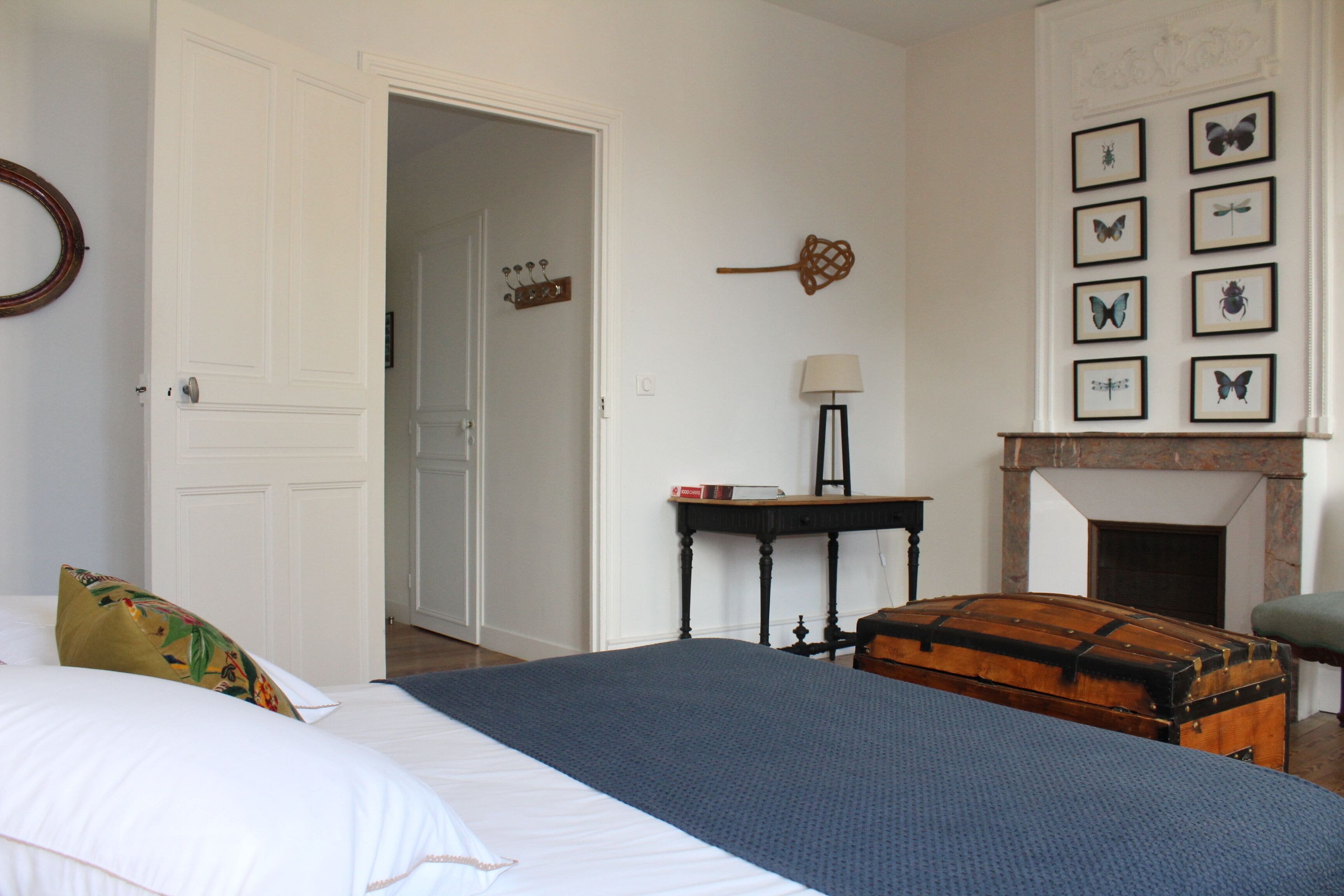 Een slaapkamer met een groot bed, een houten kist, een open haard en wanddecoraties met vlinder afbeeldingen.