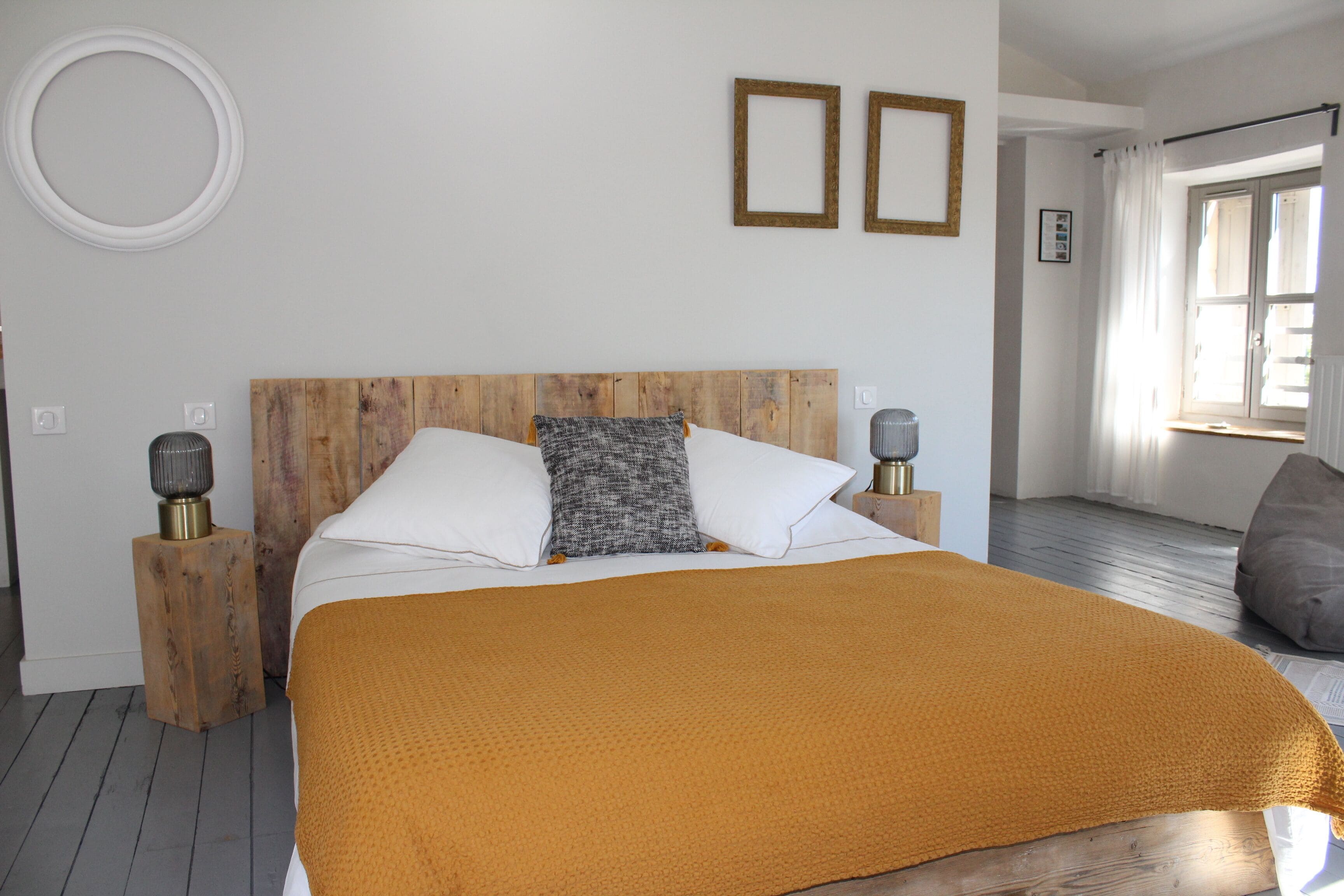 A bedroom with a wooden headboard, a large bed with white and gray pillows, a mustard-colored blanket, and two bedside lamps.